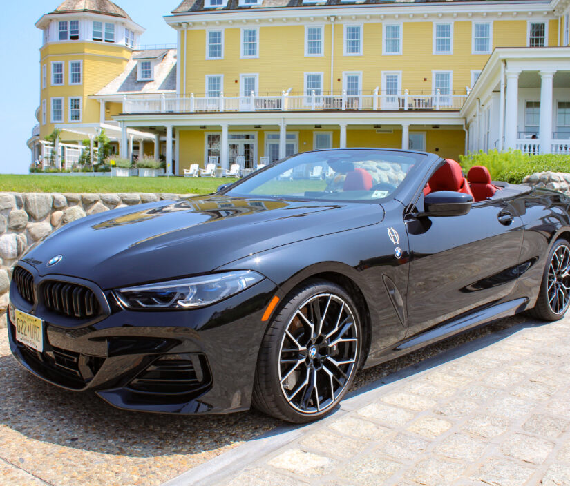 A black convertible BMW parked on a cobblestone driveway in front of a large yellow building.