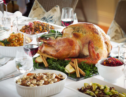 A Thanksgiving dinner table featuring a roasted turkey, side dishes, red wine glasses, and an elegant table setting.